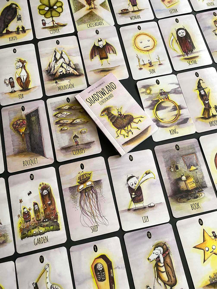 A spread of illustrated tarot cards from Schiffer Publishing, Ltd.’s Shadowland Lenormand deck features whimsical, spooky art—like the fox, mountain, and owl—plus a central Shadowland Lenormand booklet, perfect for shadow work or cartomancy.