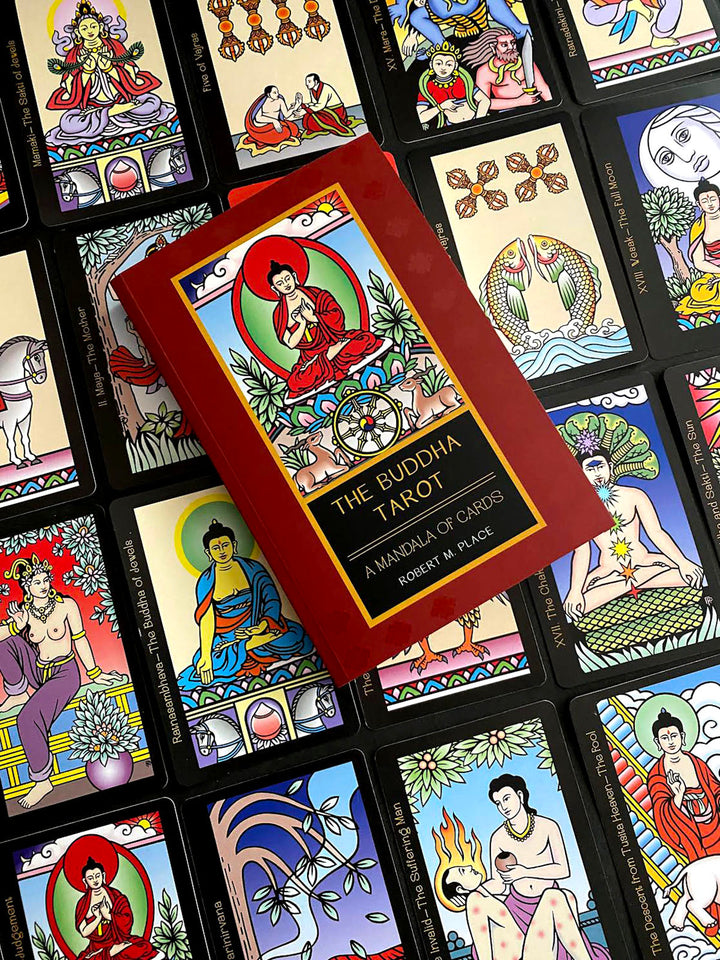 A red box labeled The Buddha Tarot by Schiffer Publishing, Ltd. rests on vibrant tarot cards, each adorned with Buddhist-inspired art, Major Arcana themes, and symbols reflecting the journey to enlightenment.