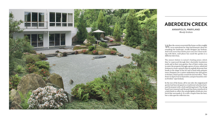 A modern white house overlooks a minimalist Japanese-inspired garden, featured in Private Gardens of the Potomac and Chesapeake by Schiffer Publishing, Ltd., with raked gravel, large stones, lush greenery, and a cozy umbrella-shaded seating area.