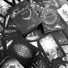 A black and white image displays the Nightfall Tarot by Schiffer Publishing, Ltd., featuring its deck box surrounded by all 78 uniquely illustrated cards arranged in a scattered Rider-Waite-Smith-inspired pattern.