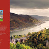 A scenic view of a river winding through hills with castle hotels in Germany. On the left, a red panel displays text about "At Home with Royalty" by Schiffer Publishing, Ltd., topped with an ornate gold crown above a castle photo.