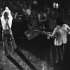 Black and white photo from "Teenage Wasteland" by Schiffer Publishing, Ltd.: a rock band on a San Francisco stage, echoing The Who’s Winterland era. One musician sings while another plays bass; fans watch closely, some with cameras.
