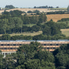 Among dense trees and rolling hills, a rectangular mass timber building with a flat roof exemplifies the environmental benefits discussed in "Innovations in Mass Timber" by Schiffer Publishing, Ltd., beneath a clear sky.
