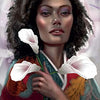 A woman with curly hair holds white calla lilies, wearing a colorful robe. Surrounded by soft blooms, she channels The Flowerwise Oracle by Schiffer Publishing, Ltd. Text: Calla Lily—Focus on the possible, let go of doubt, imagine the best.