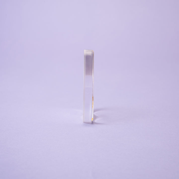 The Crystal Spirit Talking Board and Guidebook by Schiffer Publishing, Ltd. stands upright on a light purple surface against a plain purple background, its smooth, translucent form evoking the mystique of sacred crystal energy.