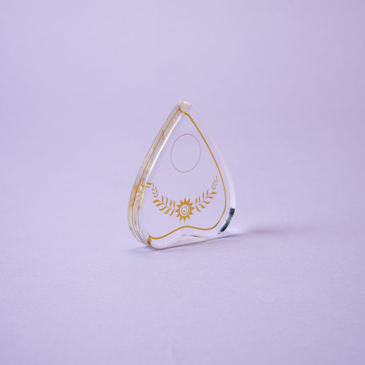 The Crystal Spirit Talking Board and Guidebook by Schiffer Publishing, Ltd. glows on a light purple background, radiating sacred crystal energy like a transparent award with gold laurel and star designs.