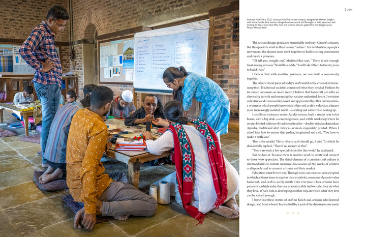 A group of adults and children gather around a low table at Somaiya Kala Vidya as a woman in blue assists, celebrating traditional artisans of India, featured in "Artisans by Design" from Schiffer Publishing, Ltd. A whiteboard is seen behind them.