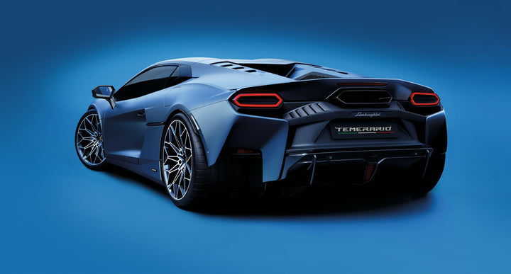 A sleek, futuristic silver sports car with angular lines and large wheels appears from the rear on a blue backdrop. The Automobili Lamborghini Special Edition by Schiffer Publishing, Ltd. boasts bold red tail lights and a "TEMPERAUD" license plate.
