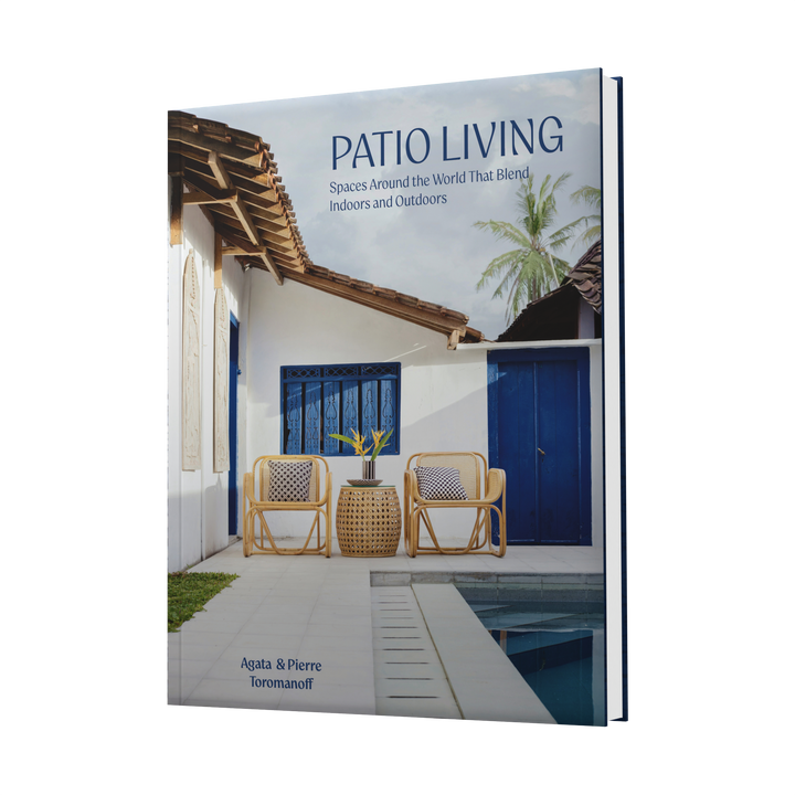Patio Living by Schiffer Publishing, Ltd. features a cover photo of a stylish patio with two wicker chairs, a small table, and potted plants—highlighting modern indoor-outdoor living against a white house with blue doors and tropical greenery.