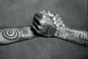 Two tattooed forearms clasp hands in a firm handshake, their bold black ink designs celebrating the rich heritage of Tahiti Tattoos by Schiffer Publishing, Ltd., highlighting the enduring power of this sacred art form.