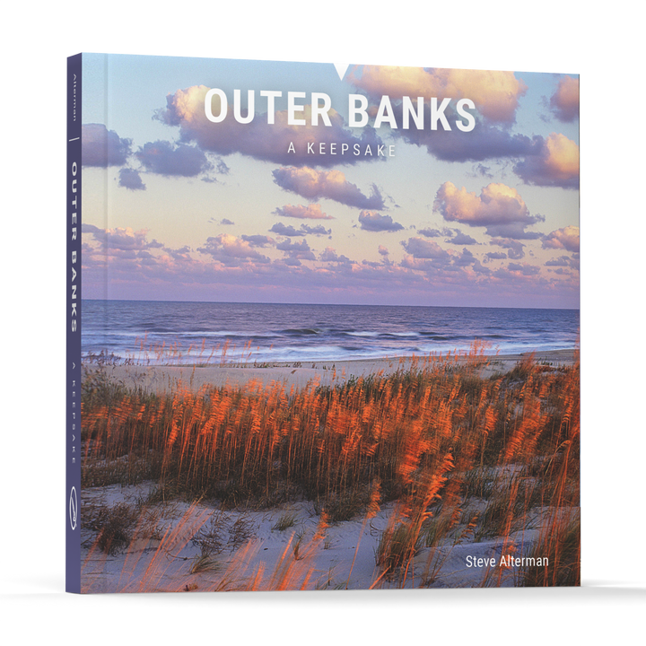 Outer Banks by Schiffer Publishing, Ltd. features a cover image of a beach with sea grass, sand dunes, and the ocean under a partly cloudy sky near Cape Hatteras in North Carolina's scenic Outer Banks.