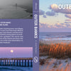 The book cover for Outer Banks by Schiffer Publishing, Ltd. features a pastel sunrise, wading birds, pier over calm sea, orange dune grasses, and iconic lighthouses of North Carolina’s Outer Banks. Back blurb describes the region. Author: Steve Alterman.