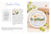 The Sunny Stitches Embroidery Kit Sunshine Pines from Schiffer Publishing, Ltd. displays a hand-embroidered landscape with pines, a river, sun, and clouds. A woven basket and green plant are nearby; supplies and instructions are shown on the left.