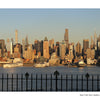 The New York City skyline viewed across the Hudson River behind a decorative iron fence, reminiscent of a souvenir photo book.