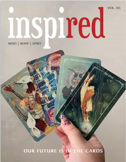 A hand with purple-painted nails holds four tarot cards against a sparkling background. The cards are featured on the cover of Inspired magazine, with the headline: OUR FUTURE IS IN THE CARDS.