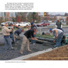 Construction workers pave a roadway with pervious concrete, as described in "Paving with Pervious Concrete" by Schiffer Publishing, Ltd., with buildings, vehicles, and trees visible in the background.