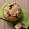A glass bowl of pear-shaped dog treats sits on a green cloth atop wood, with one treat beside it—a creative recipe idea from "Cooking for Dogs" by Schiffer Publishing, Ltd.