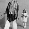 A scene from "Pueblo Dancing" by Schiffer Publishing, Ltd. shows a person in traditional Pueblo attire with ribbons facing a young girl in a white dress and veil, evoking the depth of Native American history.
