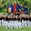 A group of U.S. Naval Academy officers in dress uniform march with the American flag on a grassy field in Annapolis, as depicted in "Annapolis Reflections" by Schiffer Publishing, Ltd.