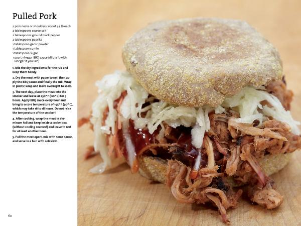 A pulled pork sandwich sits on a wooden surface, with "The Little Smoker Book" by Schiffer Publishing, Ltd. beside it—a recipe guide perfect for home smoking and beginner smokers.