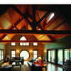 A spacious living room features Timber Frame Hybrids by Schiffer Publishing, Ltd.—exposed timber beams, vaulted ceilings, large arched windows, elegant sofas, a coffee table, and a patterned rug bathed in natural light.