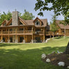 The Cedar Style by Schiffer Publishing, Ltd. features a classic log cabin with a stone chimney and wraparound porch, set on a grassy lawn with trees, landscaped rocks, and a mulch bed in the foreground.