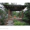 Inspired by "Diplomatic Gardens of Washington" by Schiffer Publishing, Ltd., a wooden pavilion with a tiled roof sits amid lush greenery and rocks, sheltering four wooden chairs and a small table in a private garden.
