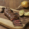A juicy grilled steak from "Pure Steak" by Schiffer Publishing, Ltd., sliced to show a pink center, served with baked potatoes and yellow cheese—ideal inspiration for steak cookbook fans or beef cut enthusiasts.