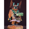 The Hopi Kachinas by Schiffer Publishing, Ltd. features a wooden doll adorned with a detailed mask, vibrant attire, feathers, and accessories like a corn cob and rattle, standing on a wooden base against a dark background.