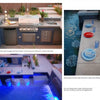 Inspired by *New Ideas for Living Outdoors* by Schiffer Publishing, Ltd., this sleek outdoor kitchen with grill, sink, and storage beside a glowing pool features blue mosaic tiles and chic tableware for ultimate backyard style and relaxation.