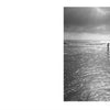 East Coast Atlantic Beaches" by Schiffer Publishing, Ltd.: A serene black-and-white photo shows two people in shallow water, gazing at the ocean under a cloudy, sunlit sky. The elegant scene is beautifully framed with a wide white border.