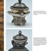 Tibetan Artifacts by Schiffer Publishing, Ltd.: Two ornate antique silver kapalas with lids—one on a round tripod base with faces, the other on a square base with lion and floral motifs—are photographed on a light background.