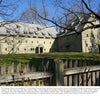Lancaster County Reflections by Schiffer Publishing, Ltd. captures a classic scene—a large, historic yellow barn with multiple gabled roofs behind a wooden picket fence in a grassy yard, framed by bare trees beneath a clear blue sky.