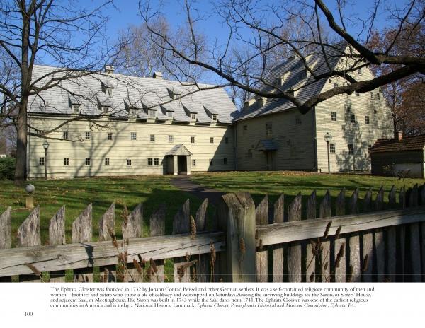 Lancaster County Reflections by Schiffer Publishing, Ltd. captures a classic scene—a large, historic yellow barn with multiple gabled roofs behind a wooden picket fence in a grassy yard, framed by bare trees beneath a clear blue sky.