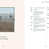 On a sandy Devon beach, someone watches two surfers and Nell, a black Labrador, head for the waves. The left page of "Conversations with Nell" by Schiffer Publishing, Ltd. reads "Chapter 18: Surf Chasing"; the right has script-style dialogue.