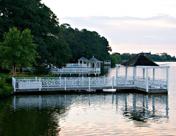 Rehoboth Reflections by Schiffer Publishing, Ltd. captures serene white wooden gazebos and a pier stretching over a calm lake, surrounded by lush trees like those at Delaware seashore resorts, beneath a soft, cloudy sky.