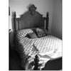 Black and white photo of a neatly made bed with a patterned quilt and a tall, ornate wooden headboard, evoking the mysterious charm of Maryland legends from "Ghosts of Maryland" by Schiffer Publishing, Ltd. Sunlight highlights the bed’s shape and texture.