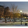 People ice skating at an outdoor rink in a snowy city park at dusk, with string lights, street lamps, and Boston landmarks featured in "Boston Wide" by Schiffer Publishing, Ltd., evoking a panoramic Boston winter scene.