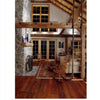 A cozy living room inspired by "Barn Again" from Schiffer Publishing, Ltd., with vaulted ceilings, wooden beams, a stone fireplace, wood floor, rocking chairs, and a rug. French doors and warm lighting complete the inviting atmosphere.