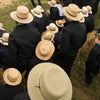 “Faces of Lancaster County” by Schiffer Publishing, Ltd. captures an evocative, artful scene of Amish life—people in black clothing and straw hats gathering outdoors on grass and hay, as seen from above—reflecting Lancaster County’s unique culture.