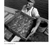 A scene from Bodine's Industry by Schiffer Publishing, Ltd. shows a man in a cap and striped shirt on a boat, holding a tray of soft shell crabs over a bucket with water in the background—a classic American image.