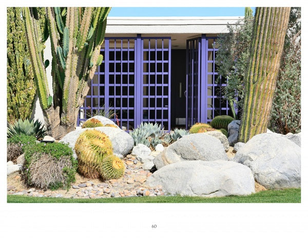 Showcasing the Palm Springs Mid-century Modern style by Schiffer Publishing, Ltd., a modern building with purple grid doors is set among large cacti, agave, rocks, a desert landscape, and green grass in the foreground.