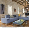 A modern King William living room, as seen in "Old Places, New Spaces" by Schiffer Publishing, Ltd., features a gray sectional, vibrant pillows, glass coffee table on wheels, art on stone walls, wood floors, and exposed beams leading to the dining area.