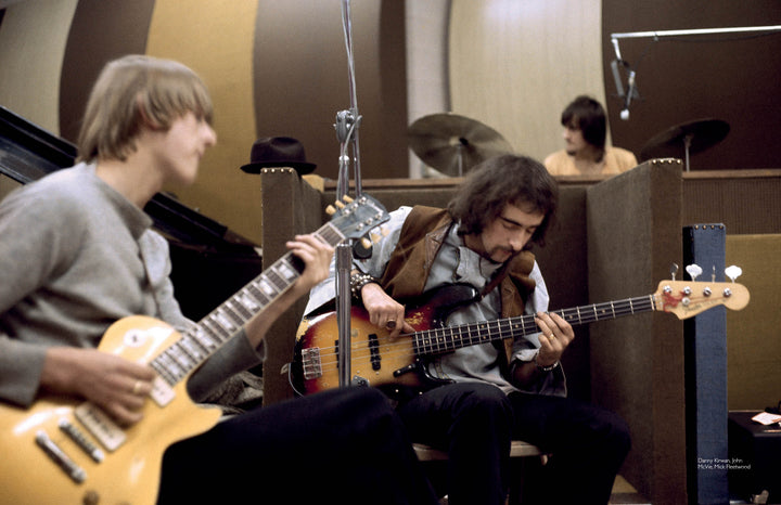 Two musicians play electric guitars and a drummer is in the background behind brown sound barriers in a casual recording studio, reminiscent of Fleetwood Mac’s blues era—just like "Fleetwood Mac in Chicago" from Schiffer Publishing, Ltd.